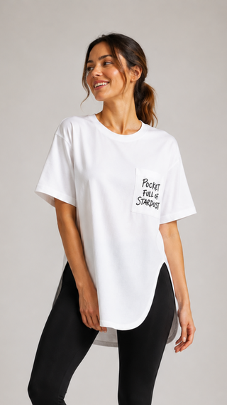 A woman modeling a white oversized t-shirt with a small black graphic text on the pocket, paired with black leggings, against a neutral light gray studio background.