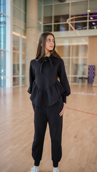 Person wearing a black outfit in an indoor setting with large windows.