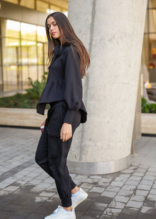 Woman in black outfit leaning against a column in an urban setting