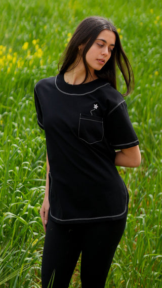 Woman wearing a black outfit with white trim standing in a field of green grass and yellow flowers.