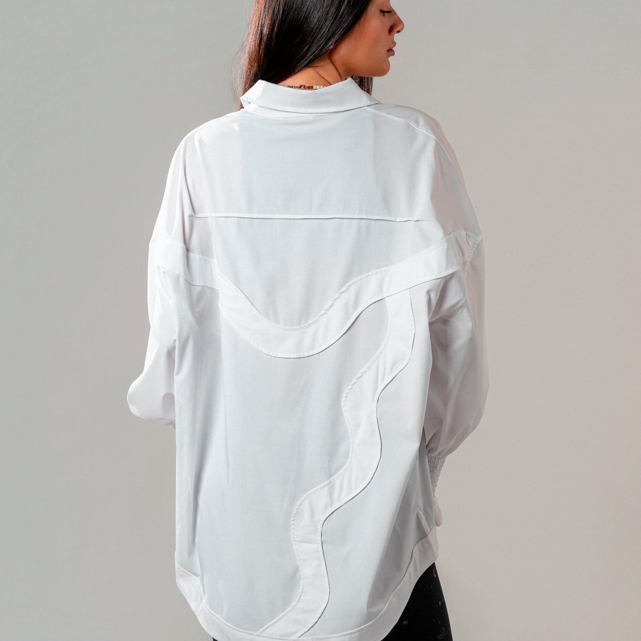 Person wearing a white oversized shirt with black pants on a plain background